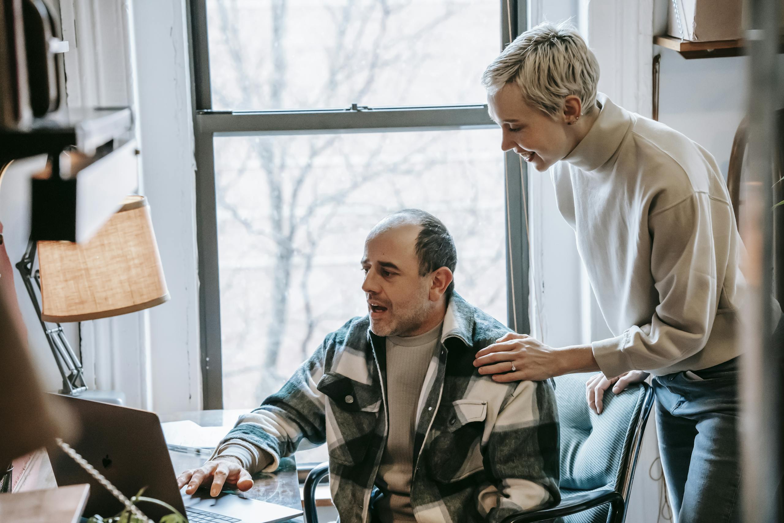 Cheerful colleagues working together on a laptop in a bright workspace.
