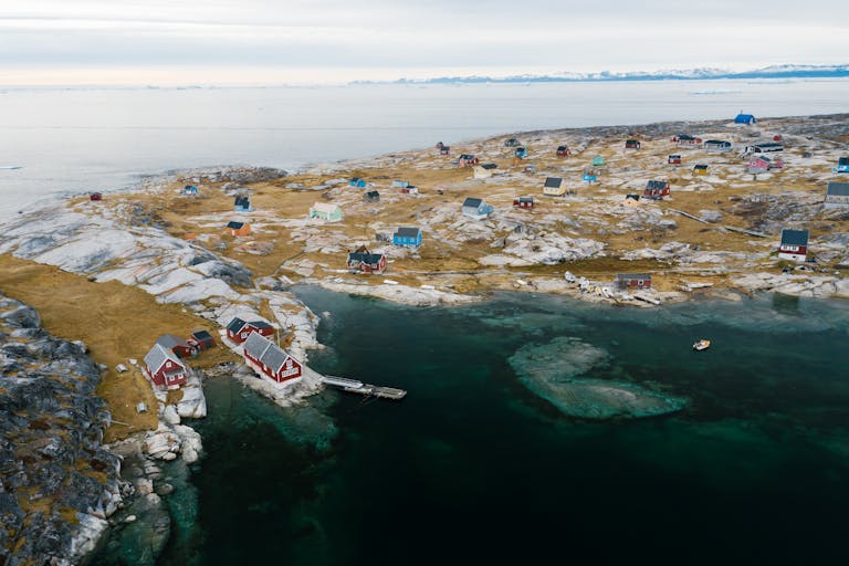 A beautiful aerial shot of a remote coastal village in winter, showcasing colorful houses and rocky landscape.